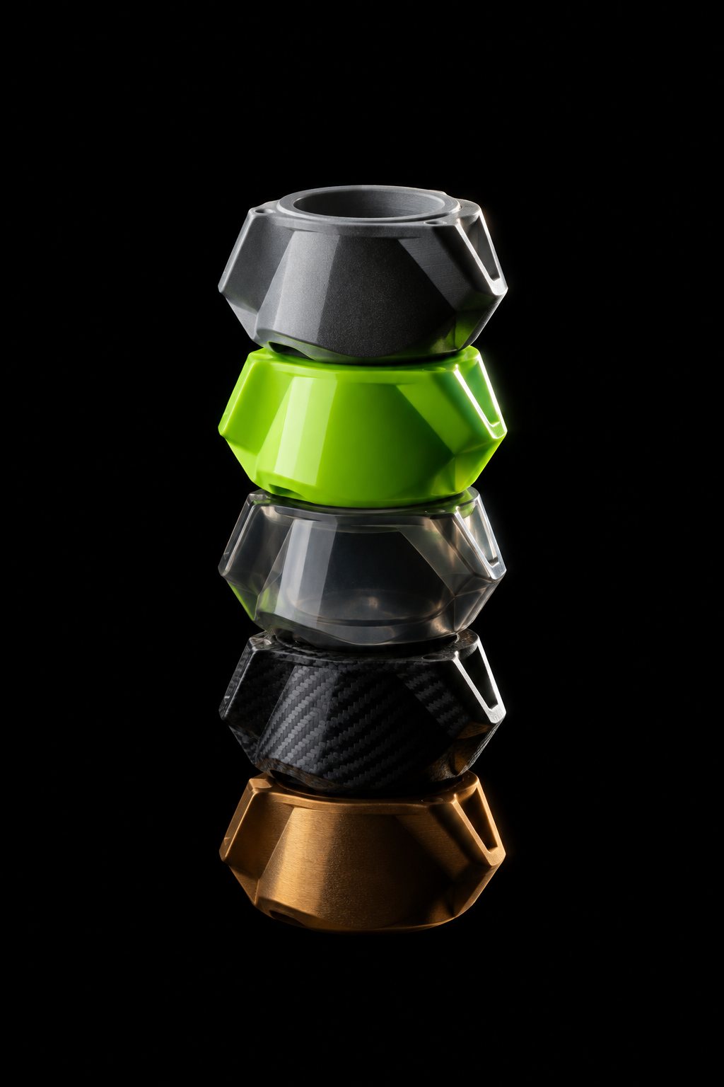 A mesma peça impressa em cinco materiais diferentes, empilhada: cinza fosco, verde brilhante, translúcido, fibra de carbono e bronze